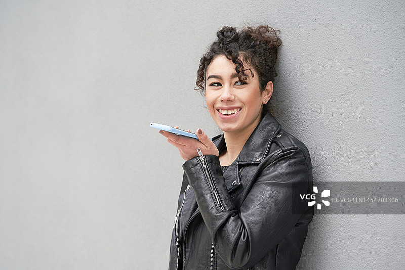 倚靠在灰色墙壁上，用手机愉快交谈的年轻金属女孩图片素材