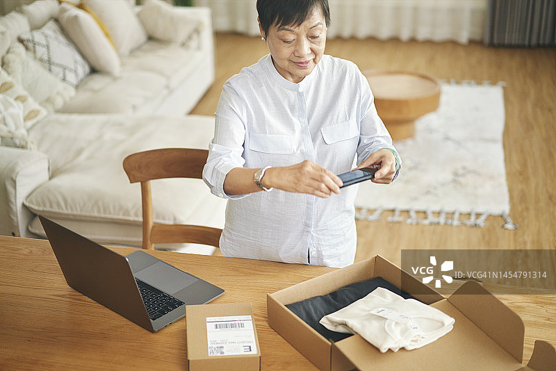一位中国老年妇女用智能手机拍摄她要打包运送给买家的物品图片素材