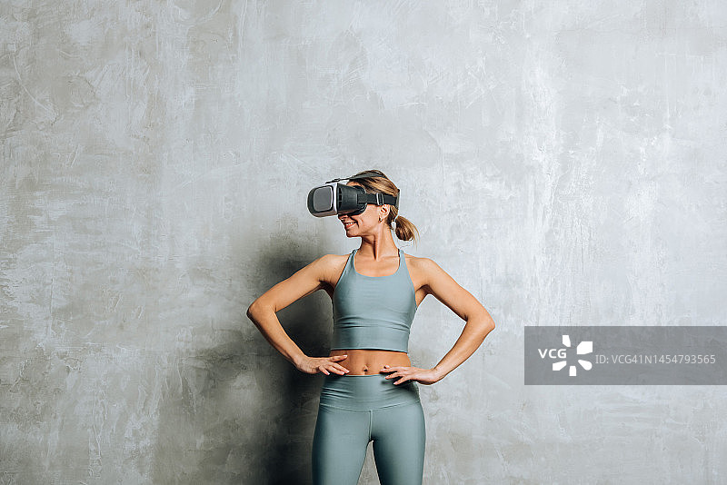 戴着VR虚拟现实眼镜的微笑女人，背景是混凝土墙图片素材