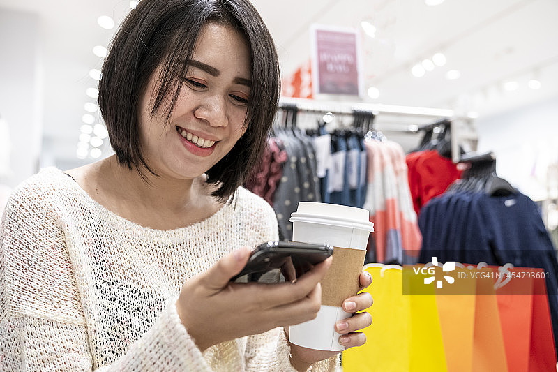 在服装店购物时使用智能手机的快乐女人图片素材