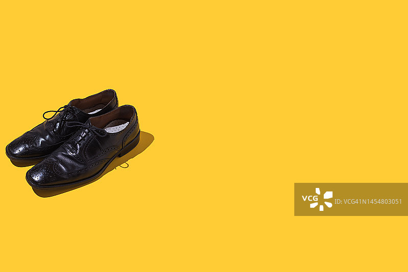 黄色背景上的一双黑色复古皮鞋，优雅男士概念图片素材