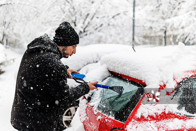 年轻男子正在清理汽车挡风玻璃上的冰雪图片素材