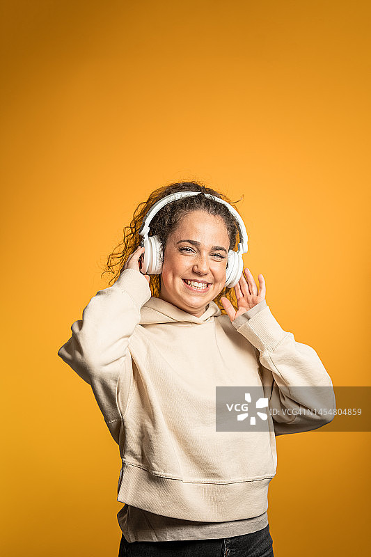 在黄色背景下戴耳机听音乐的女人图片素材