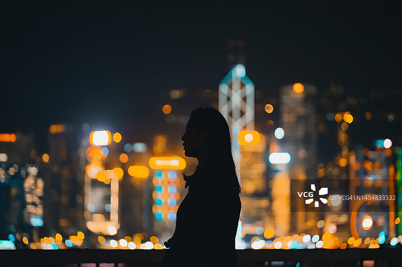 亚洲年轻女性在城市夜景背景下的剪影图片素材