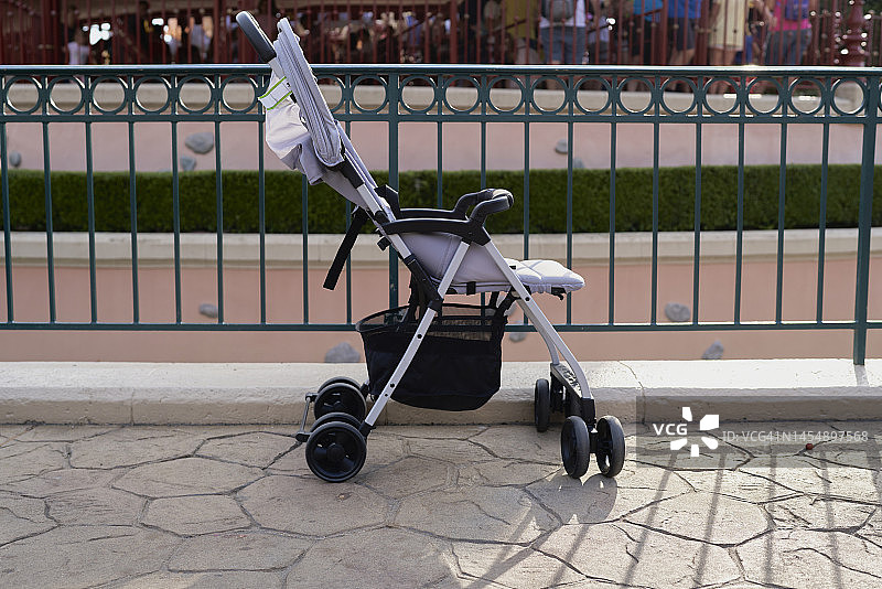 灰色婴儿车停在游乐园的栅栏旁，背景是人群图片素材