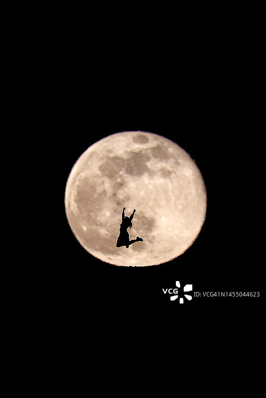 满月背景下穿裙子跳跃的女孩剪影图片素材
