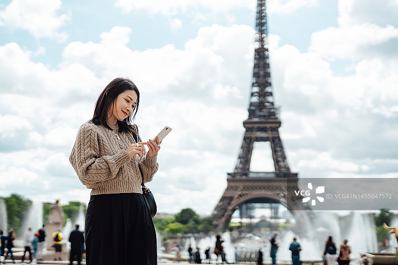 在巴黎埃菲尔铁塔前使用智能手机的年轻亚洲女性图片素材