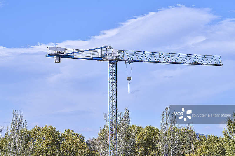 蓝色塔吊，位于树木繁茂的区域，背景是蓝天白云图片素材