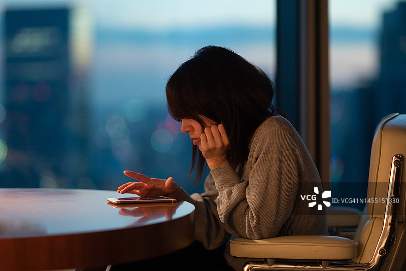 日本女人坐在桌旁用手指操作智能手机图片素材