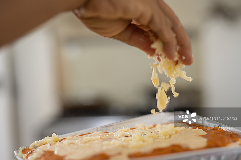 手向自制新鲜千层面中加入碎奶酪图片素材