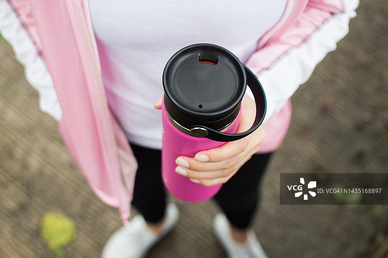 一位东南亚女性在户外跑步时用可重复使用的水瓶喝水图片素材