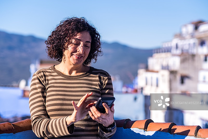 中年妇女在旅游公寓的露台上使用手机，旅行时拥有良好的数据覆盖非常重要。图片素材