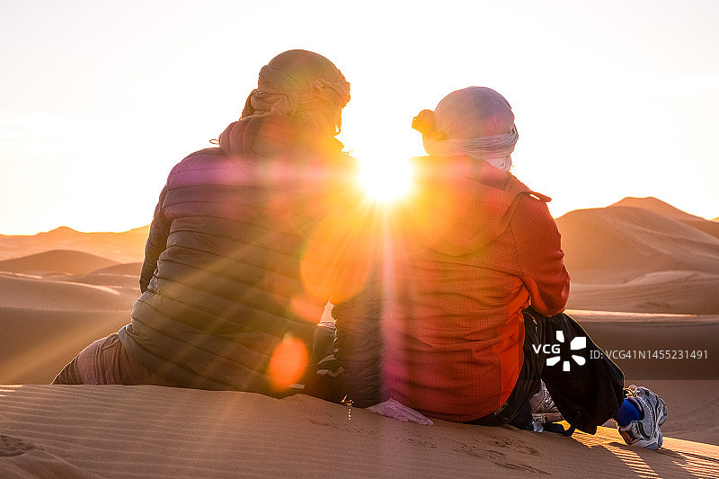 撒哈拉沙漠：两人坐在沙丘上观看日出美景图片素材