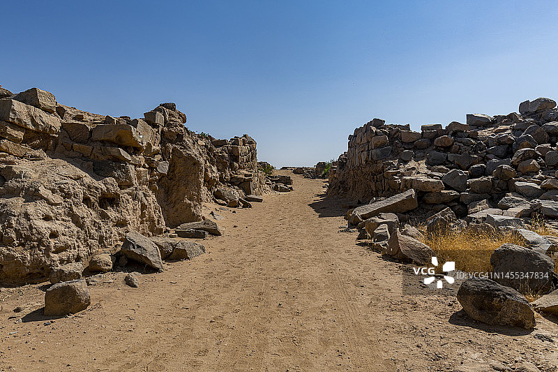 沙特阿拉伯纳季兰Al-Ukhdud考古遗址蓝天下岩石中的空土路图片素材