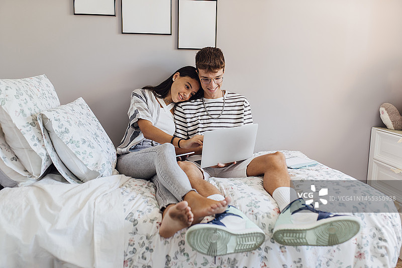 在家卧室里和哥哥一起用笔记本电脑学习的微笑女孩图片素材