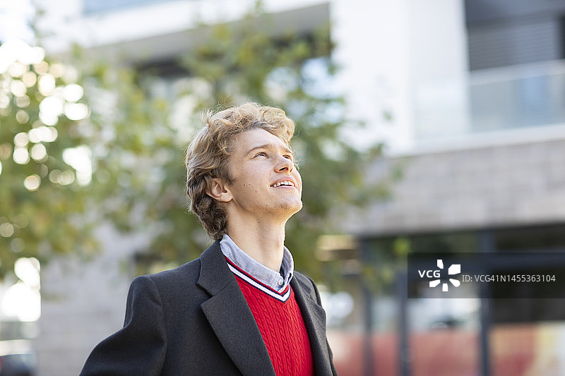 留着金色头发、身穿红色套头衫和夹克的快乐年轻人图片素材