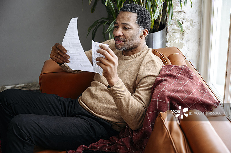 中年男人在家里的沙发上查看财务账单图片素材