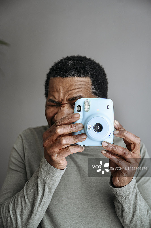 中年男人在灰墙前用立拍得相机拍照图片素材