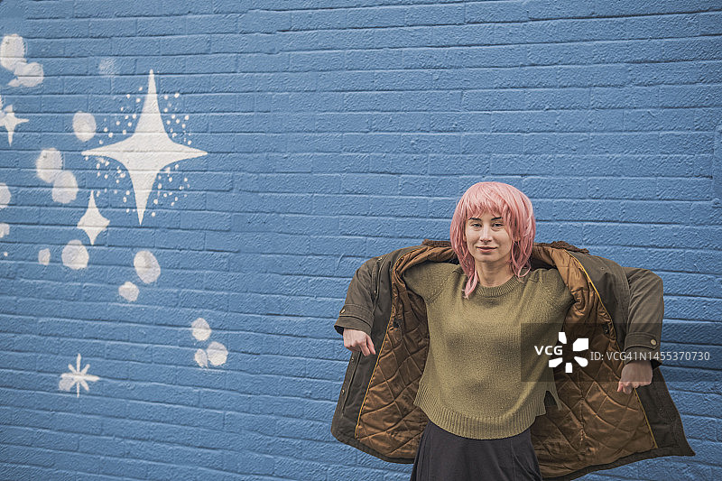 在蓝色墙前穿夹克的微笑朋克女人图片素材