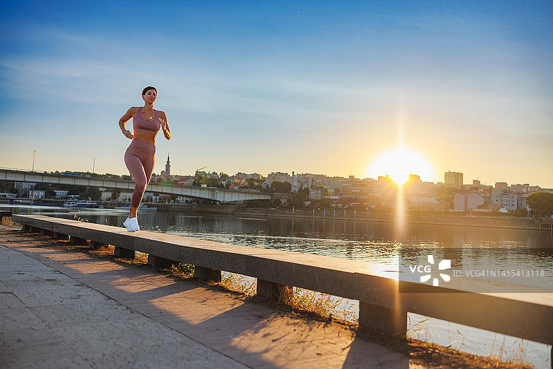 运动装女子在城市河边黎明时跑步图片素材