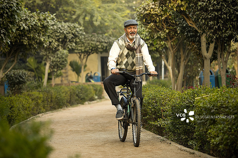 快乐的老年男人在花园小路上骑自行车图片素材