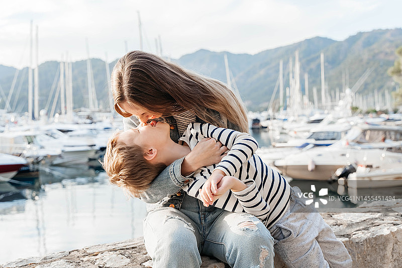 年轻的母亲和穿着条纹毛衣的小儿子在码头背景下玩耍图片素材