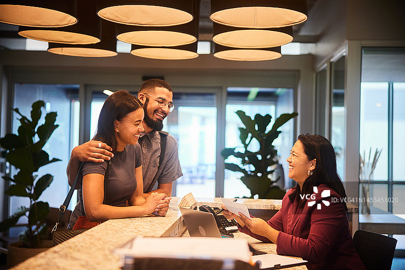 微笑情侣在酒店办理入住时与接待员交谈图片素材