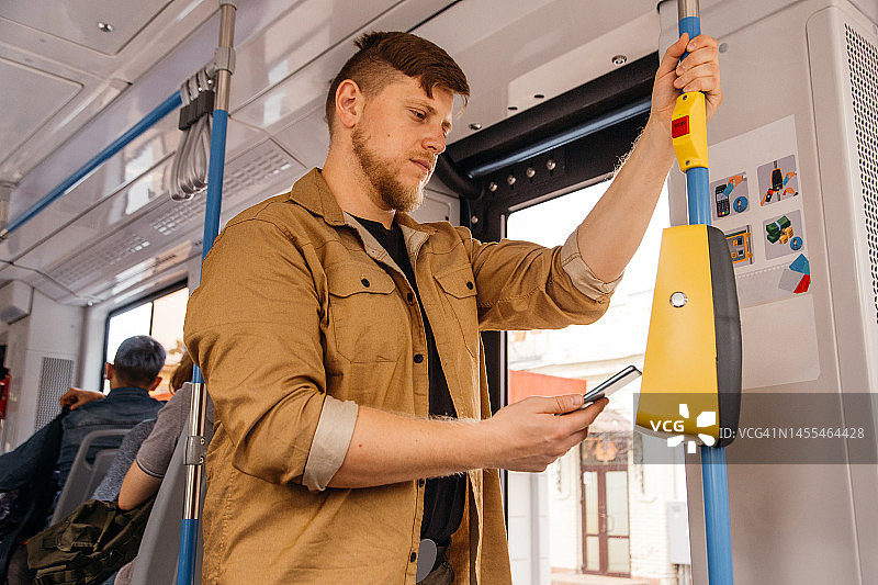 非接触式支付。年轻男人在公共交通工具上进行支付。男人用手机支付电车费用。男性通过数字钱包购买车票。图片素材