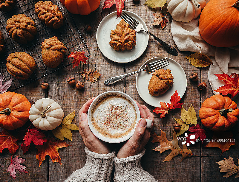 俯视秋季南瓜造型的香料蛋糕和手持拿铁图片素材