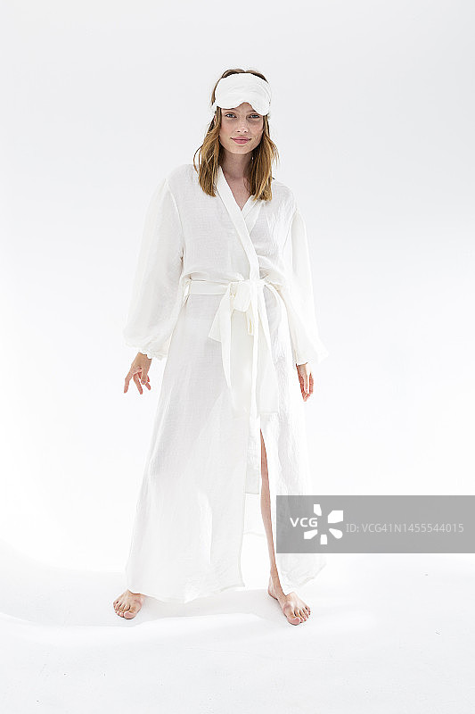 穿着白色丝绸睡衣和眼罩，看着镜头的年轻漂亮女人图片素材