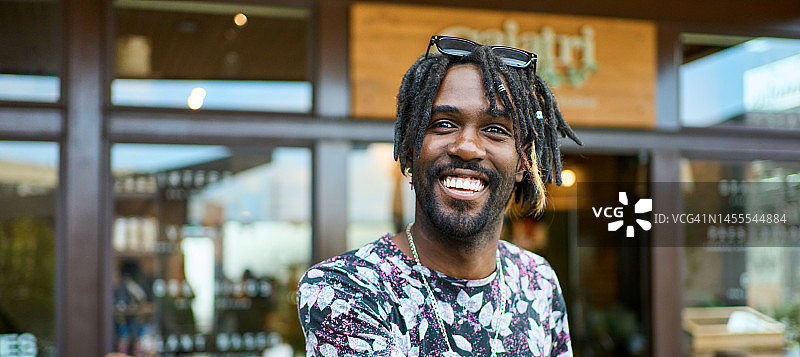 在咖啡馆露台上站立的微笑脏辫青年图片素材