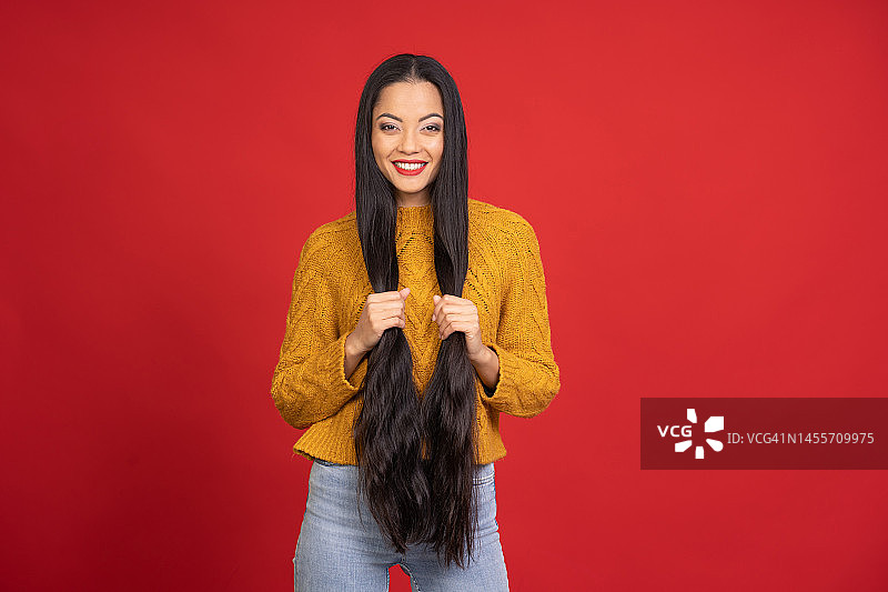 在红色背景上玩弄她黑色长发的亚洲女人图片素材