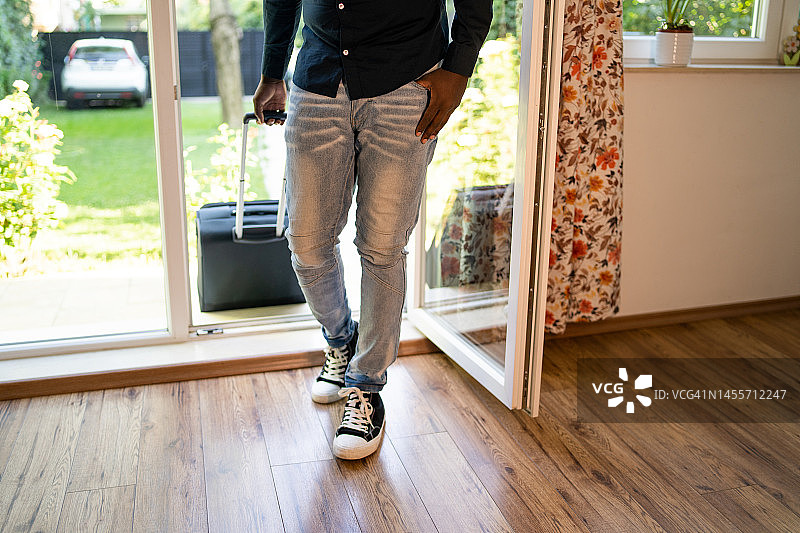 拉着轮式行李箱穿过出租屋露台门的男子图片素材