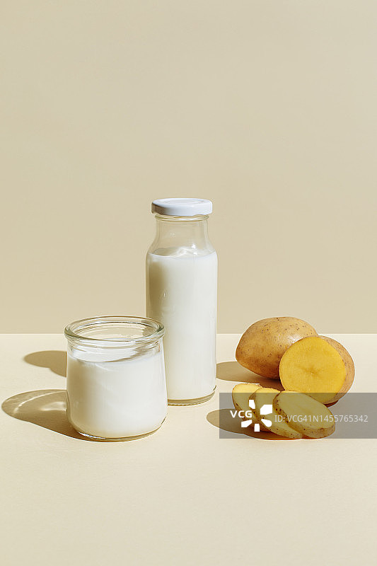 米色背景下的玻璃瓶和玻璃杯中的马铃薯植物奶，以及马铃薯块茎。健康的素食和纯素饮品概念。极简风格的无乳糖牛奶，有复制空间图片素材