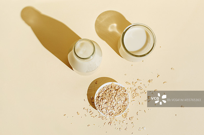米色背景上玻璃瓶和玻璃杯装燕麦奶，白色碗里的燕麦片图片素材