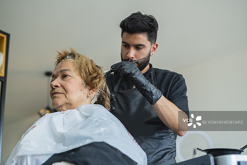 一位时髦的拉丁裔男人正在为一位年长的顾客染发图片素材