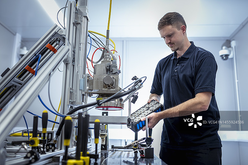 男子在汽车研究机构将汽车电池放入激光焊接机图片素材