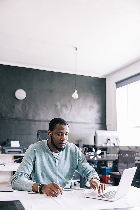 建筑师使用笔记本电脑访问3D建模软件，并在蓝图上工作，创建建筑的详细可视化效果图片素材