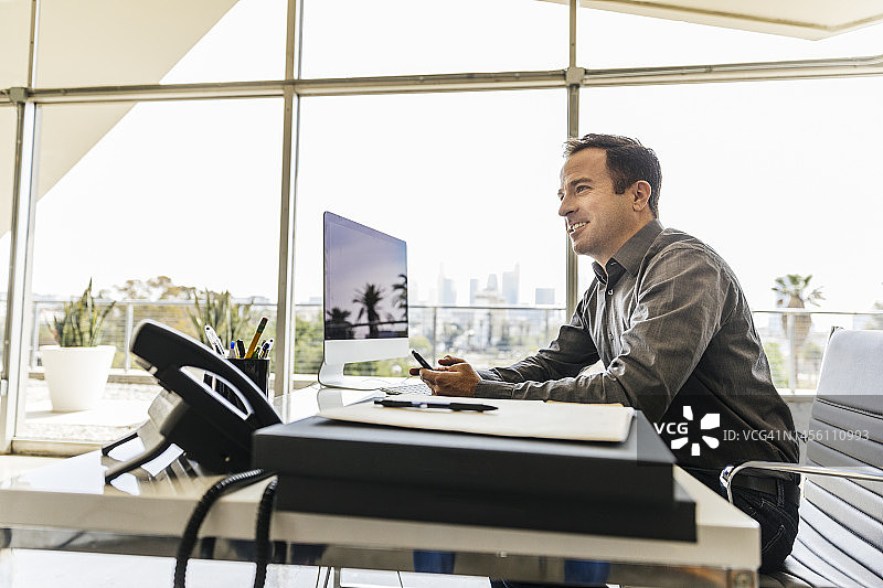 微笑的男士在办公室使用手机图片素材