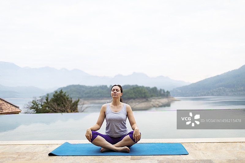 年轻女子在旅游胜地游泳池附近练习瑜伽图片素材