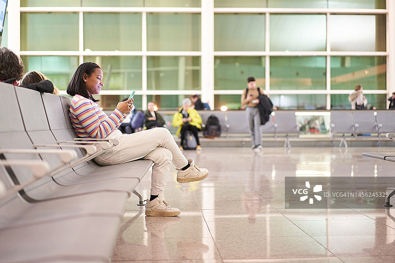 在机场候机室用手机的快乐拉丁女人图片素材