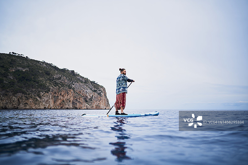 留着胡须的男人在阴天平静的海面上划桨板的侧视图图片素材