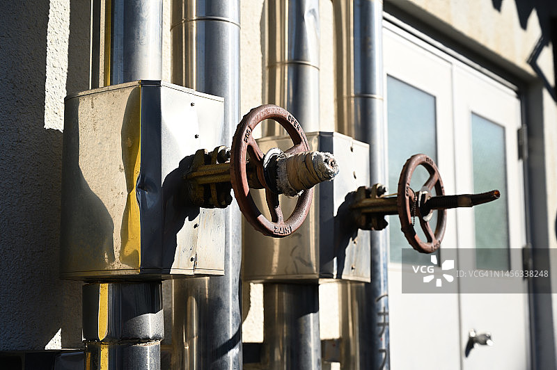 两个生锈的旋转阀门并排，后方可见垂直管道和门图片素材