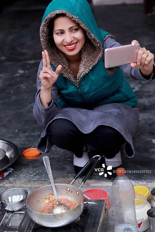 印度年轻女性在厨房准备食物，同时使用手机图片素材