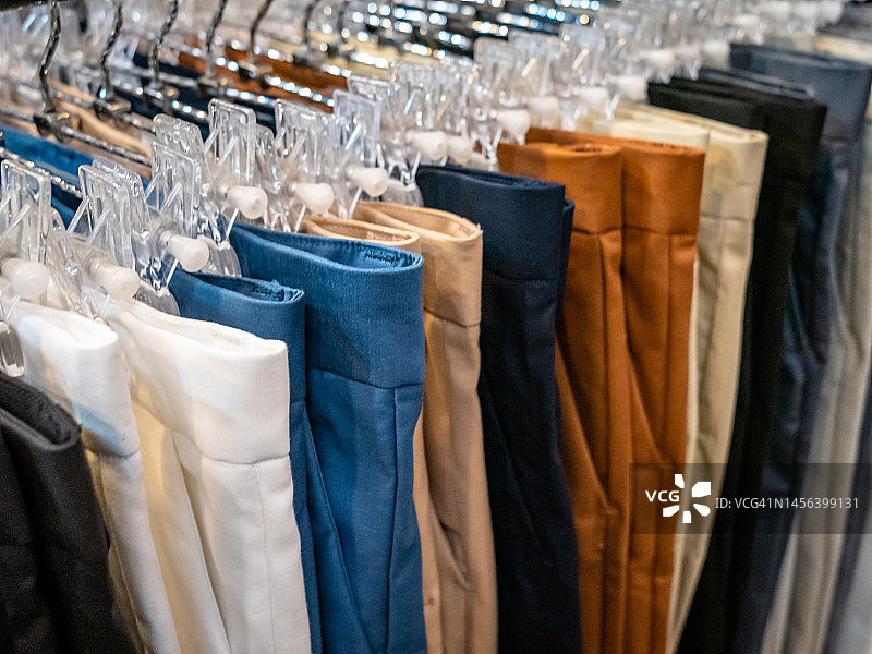 英国伦敦百货商店的衣架和架子上堆放的裤子特写，原色水洗和泥土颜色和图案的普通标准款式衬衫图片素材
