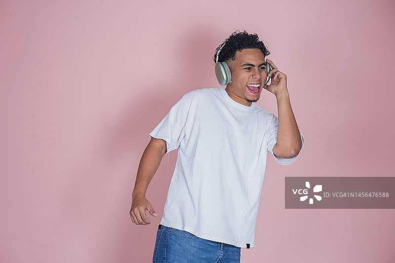 年轻的非裔美国男子戴着耳机听音乐，在粉色背景下跳舞图片素材