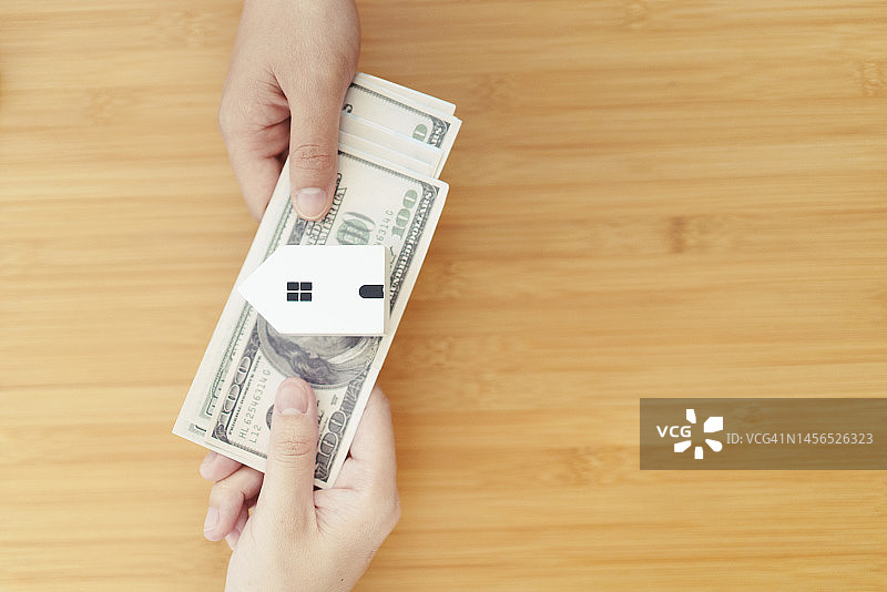 两手交换钱现金与小房子房屋贷款和房地产概念图片素材