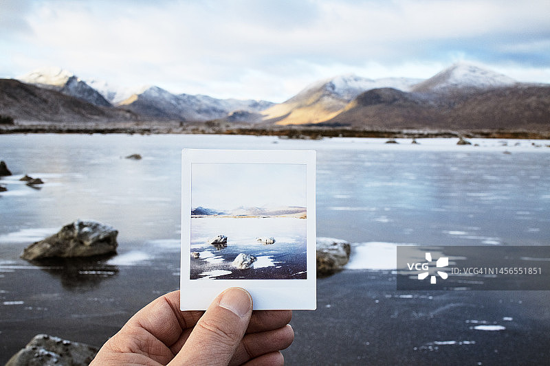 男子在苏格兰高地冬季风景前手持快照图片素材