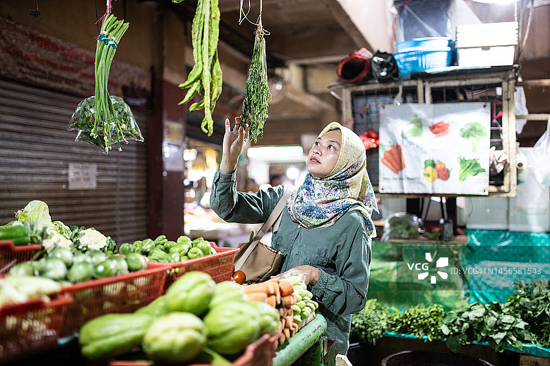 戴着头巾的美丽女人在传统市场购物，手里拿着蔬菜图片素材