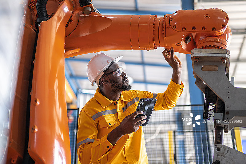 用平板电脑检查机器人手臂并在制造过程中工作的非洲工程师图片素材
